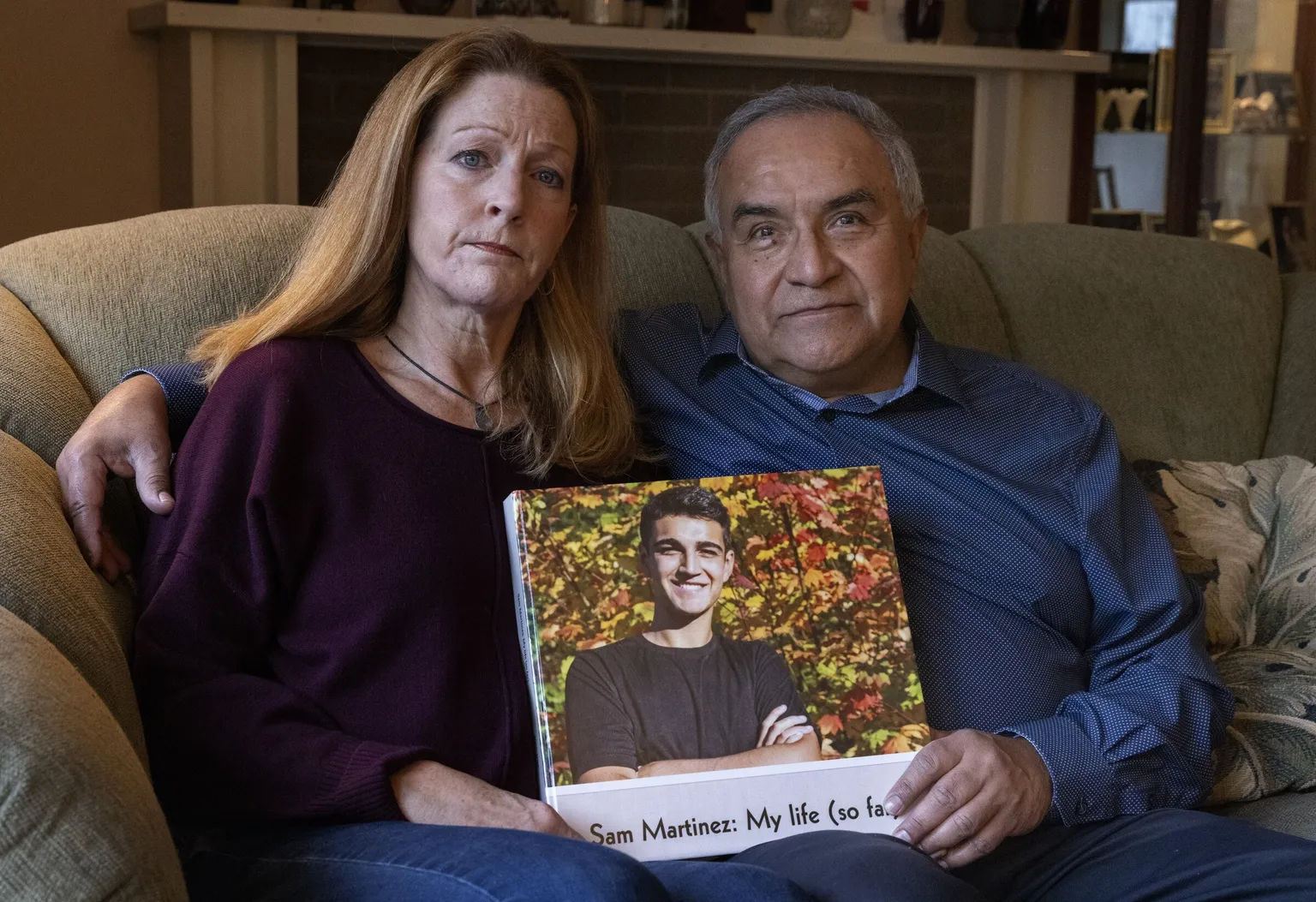 Sam Martinez's parents seated together, holding a photo book of their son titled “Sam Martinez: My life (so far)”