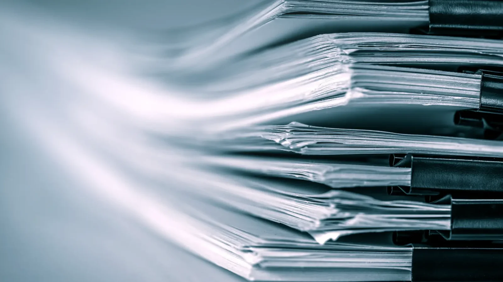 An abstract, close-up view of several thick files and documents held together by large black binder clips, emphasizing a large volume of paperwork.