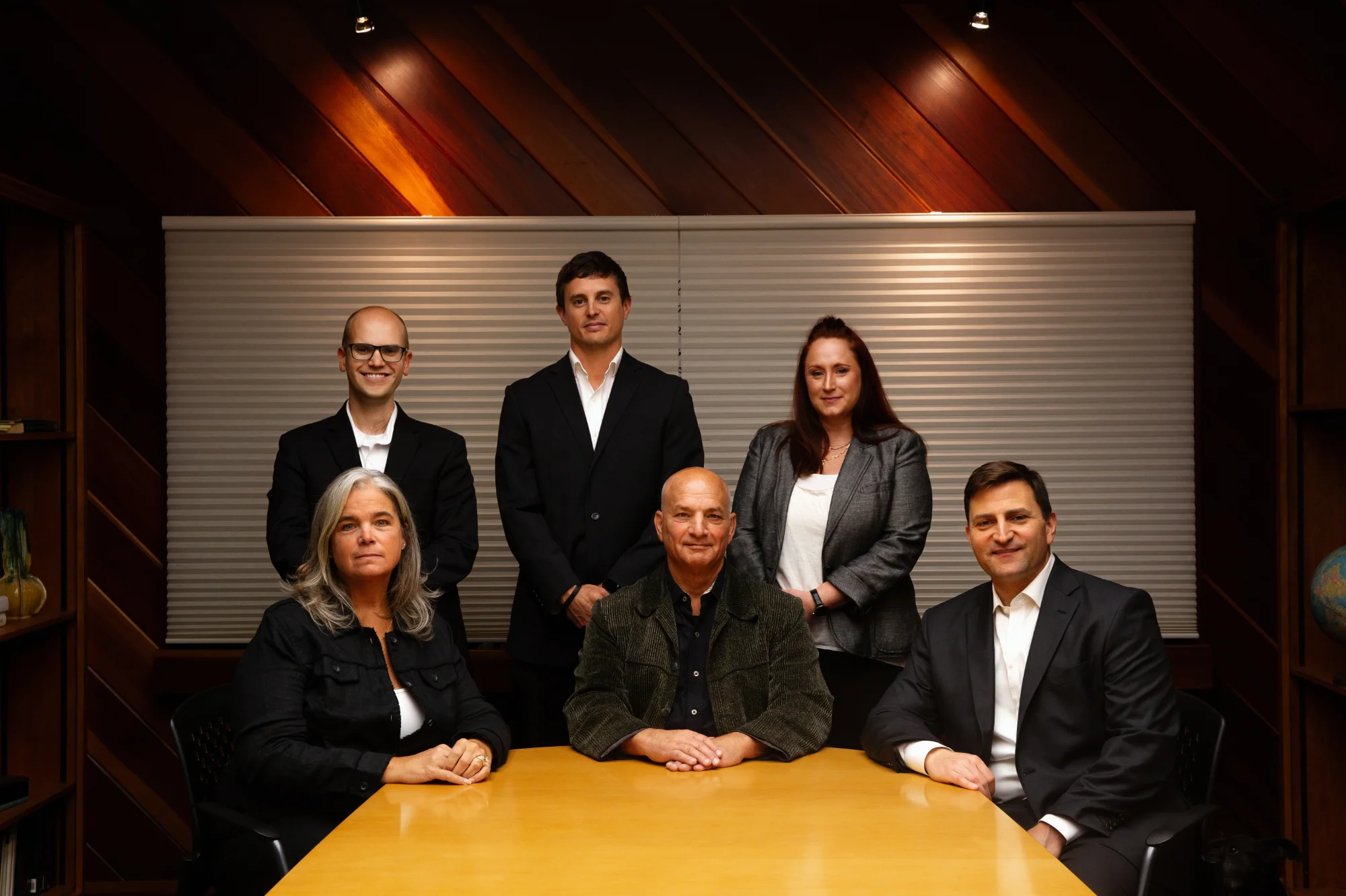 The Fierberg National Law Group team (three men, three women) pose formally around a large wooden conference table in a professional setting.