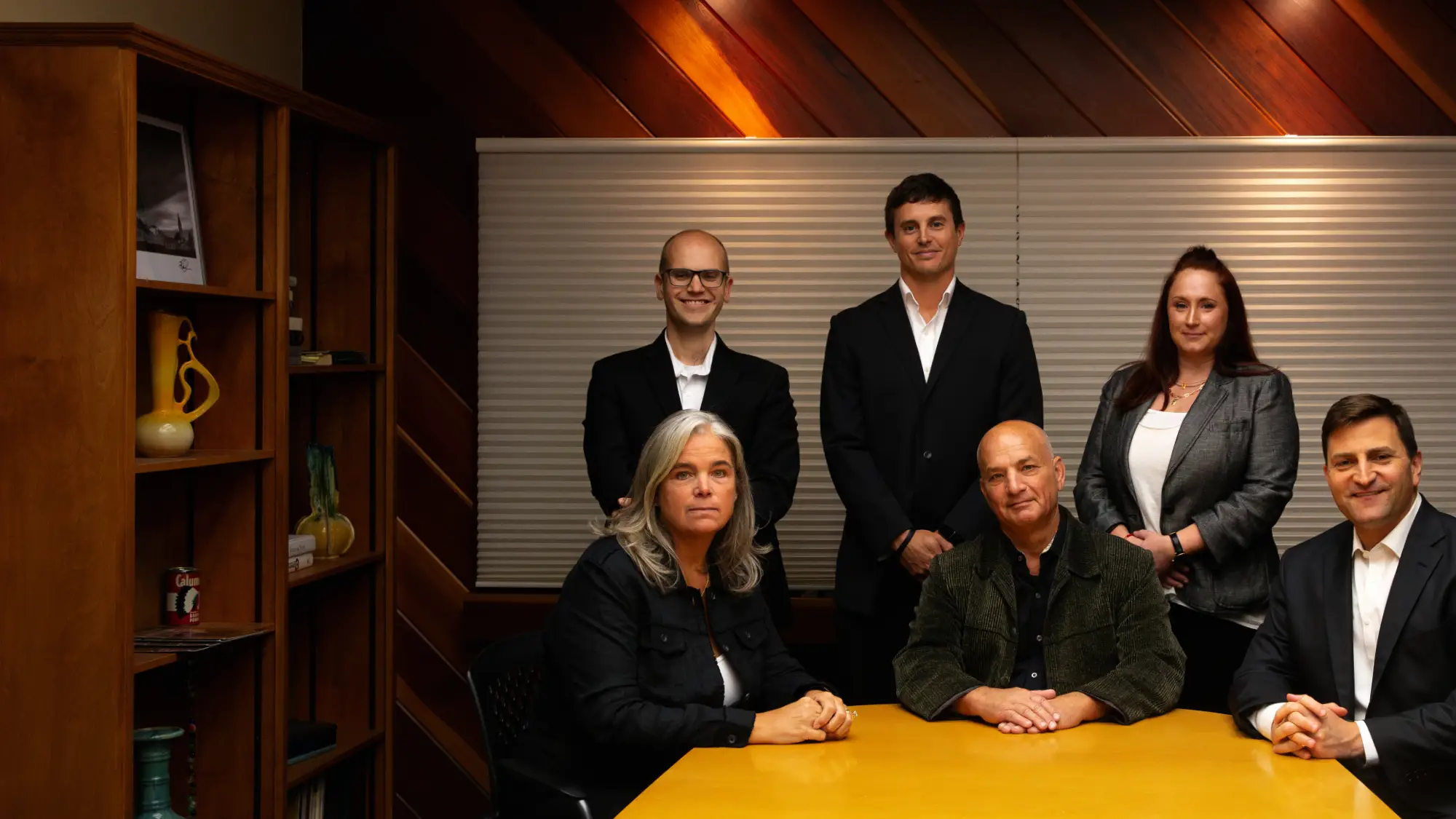 The Fierberg National Law Group team, six team members (three standing, three seated) around a yellow conference table in a sophisticated wooden office.
