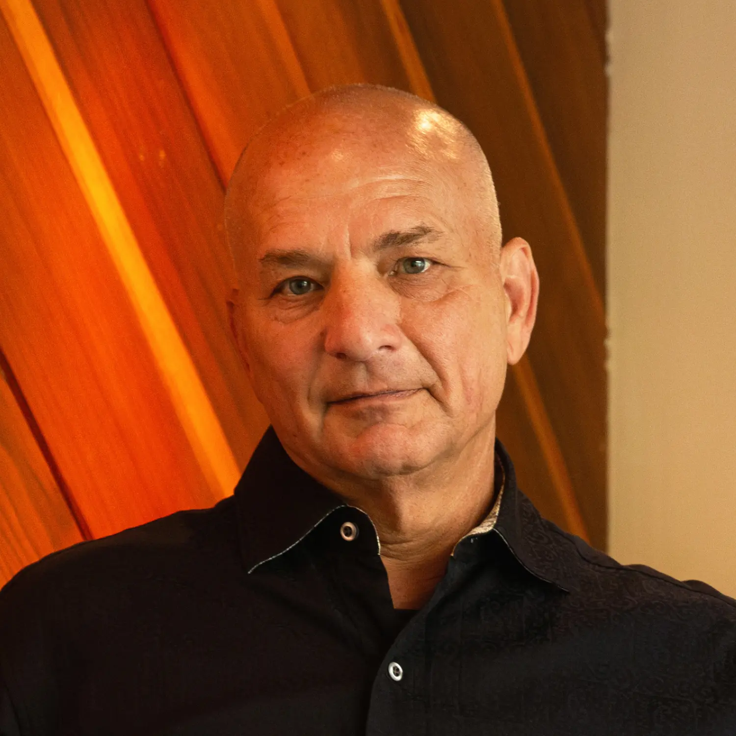 Attorney Douglas Fierberg, a bald man in a dark collared shirt, looks forward with a steady expression against a backdrop of vertical orange wood slats.