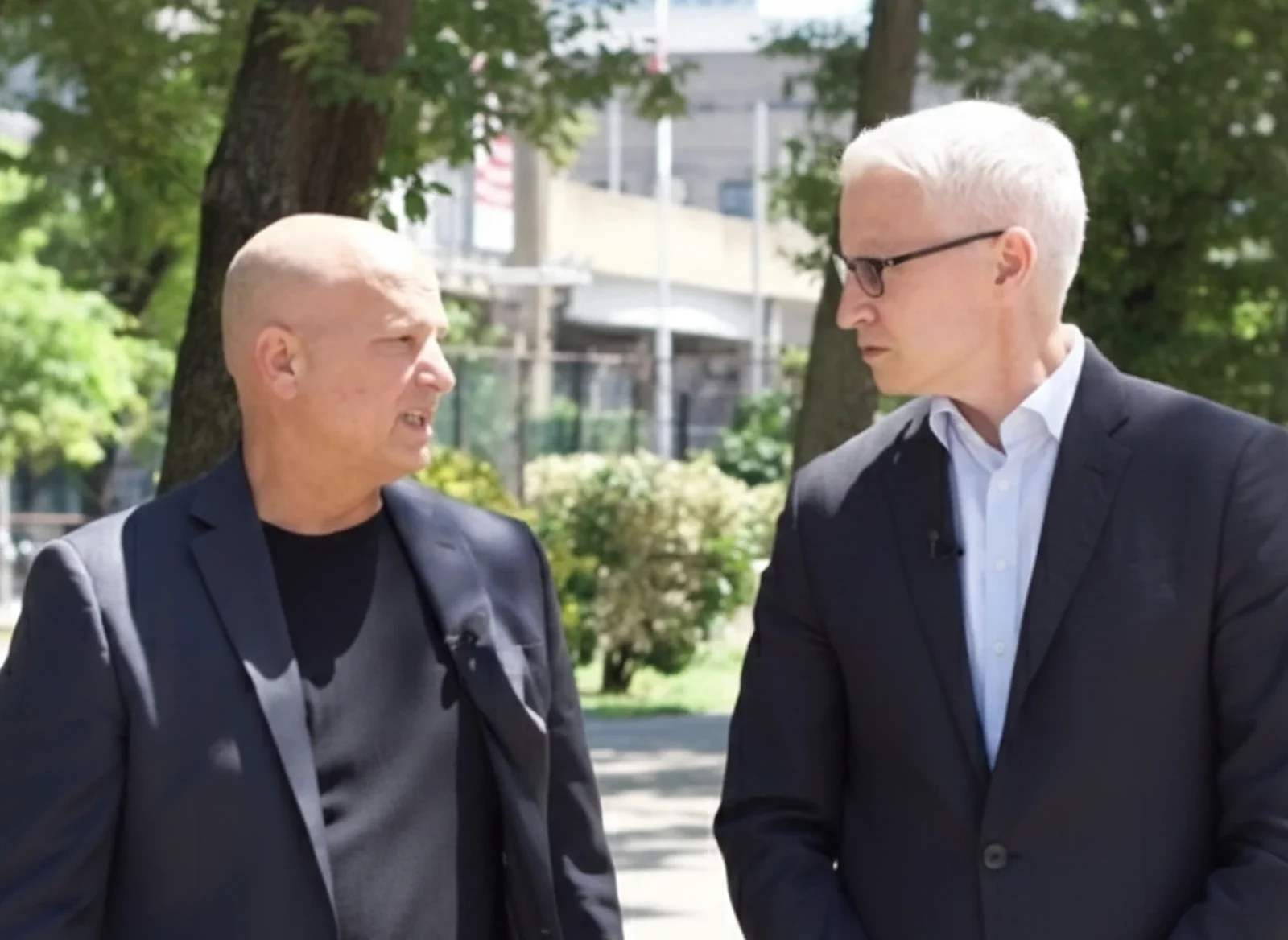 Attorney Doug Fierberg speaks to Anderson Cooper, who is wearing glasses and listening intently. Both men are outdoors in dark suits.