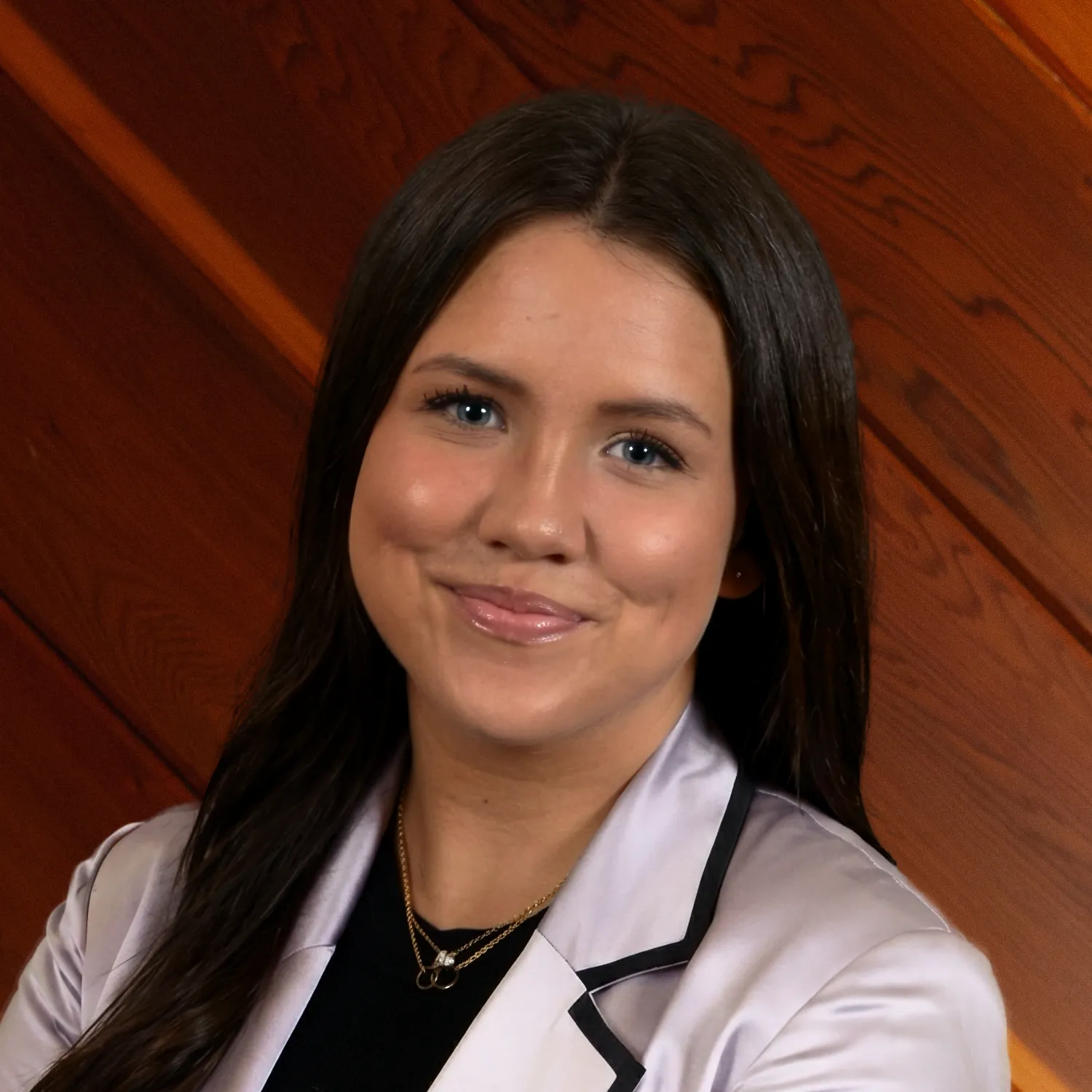 A professional headshot of Gabrielle Lewis smiling warmly. She has long dark hair and wears a white satin blazer with black trim.