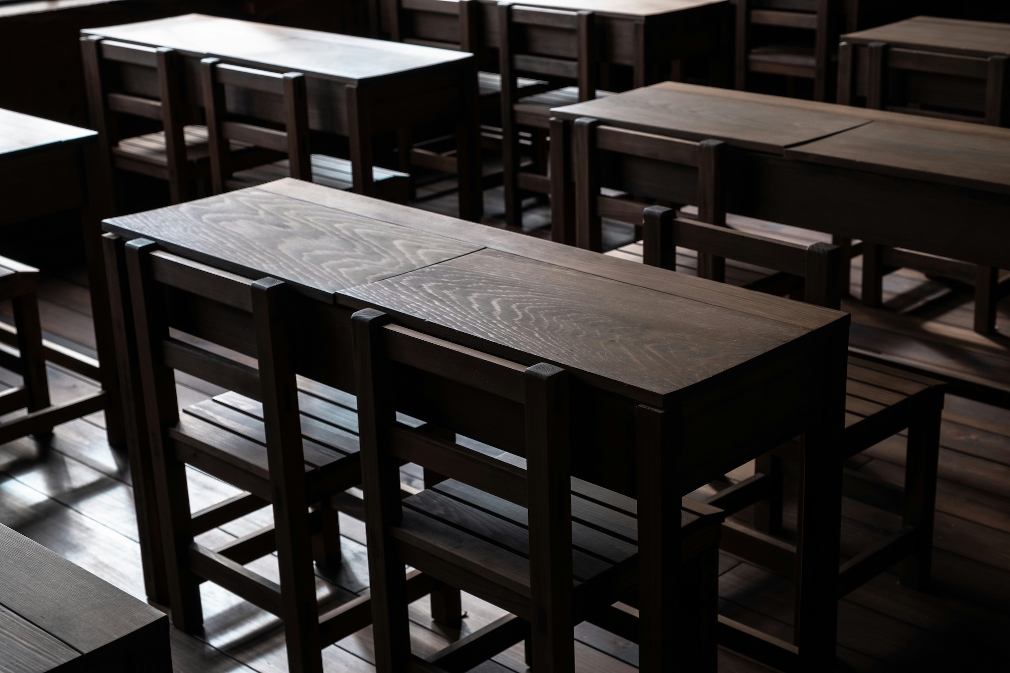 An orderly conference or training room featuring rows of dark wooden tables and chairs.
