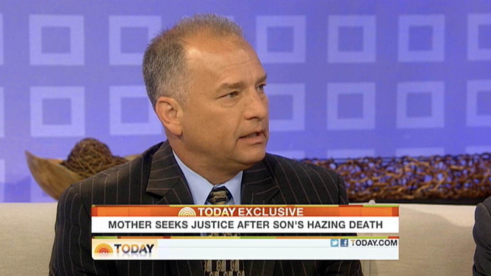 Doug Fierberg in a dark pinstripe suit and light blue shirt speaks on a television set, looking focused. An on-screen banner reads, "Mother seeks justice after son's hazing death."