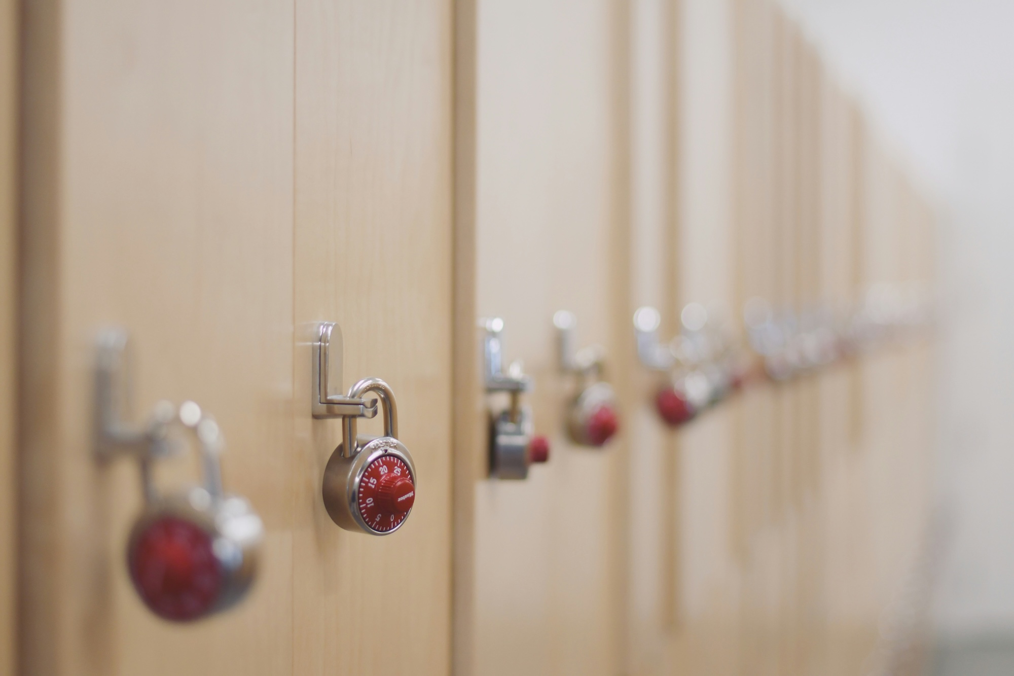 A long row of secure light wood lockers, each secured with a silver padlock featuring a distinctive red combination dial.
