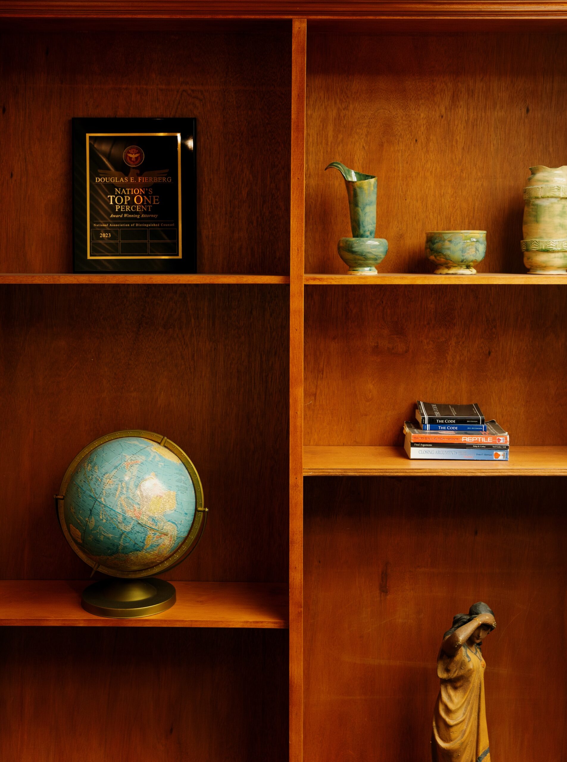 Douglas E. Fierberg's wooden office bookshelf displays his "Top One Percent Attorney" award, a globe, law books, and green pottery.
