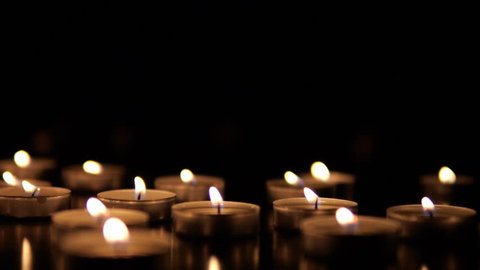 Several small, lit tealight candles are clustered together, providing a warm glow in an otherwise pitch-black environment.