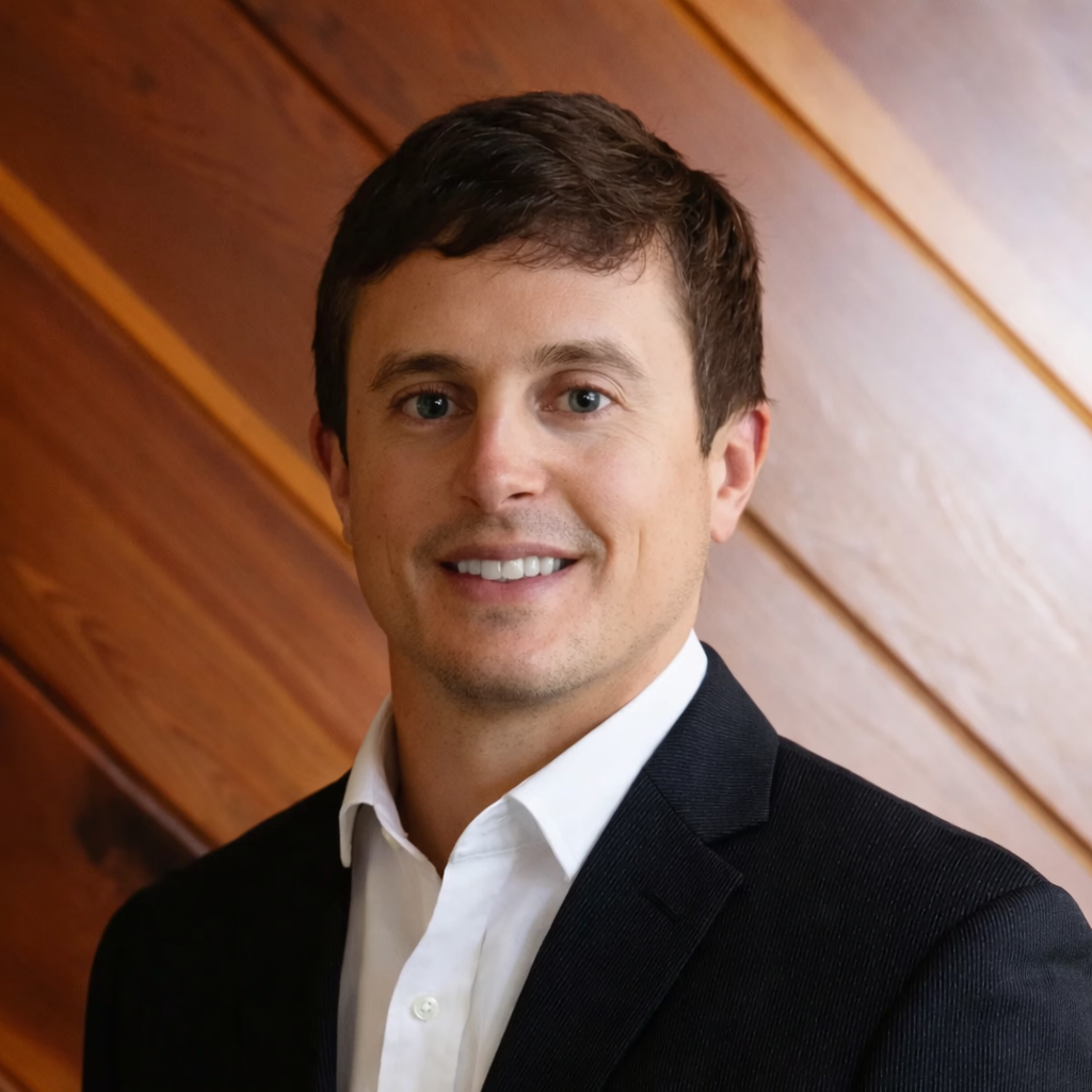 Attorney Bailor Bell poses for a professional portrait. He wears a black suit and white shirt against a diagonally aligned, warm wood-paneled background.