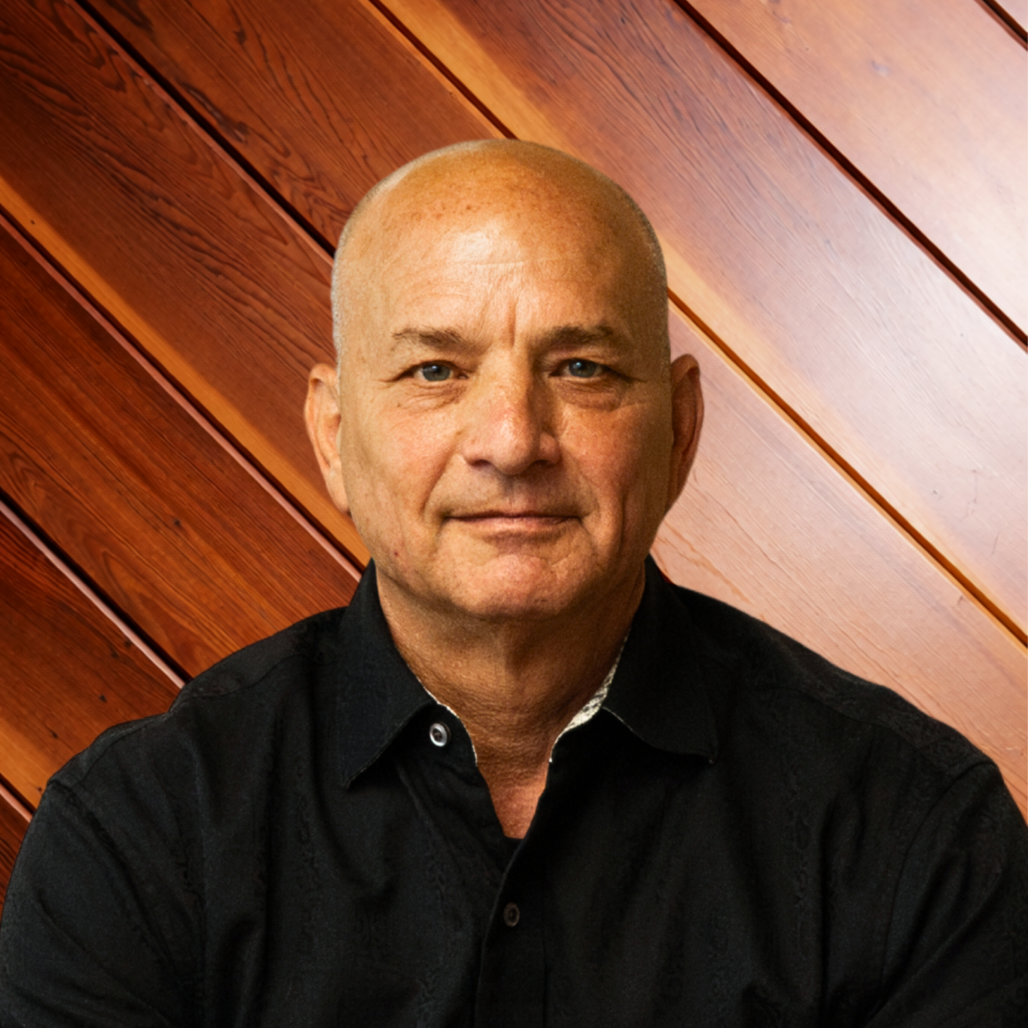 Doug Fierberg, an attorney in a black shirt stands confidently, leaning on a wooden counter with striking diagonal wood paneling behind him.