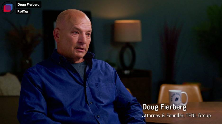 Doug Fierberg, Attorney and Founder, sits wearing a blue shirt, speaking with a serious and engaged expression in a dimly lit office setting.
