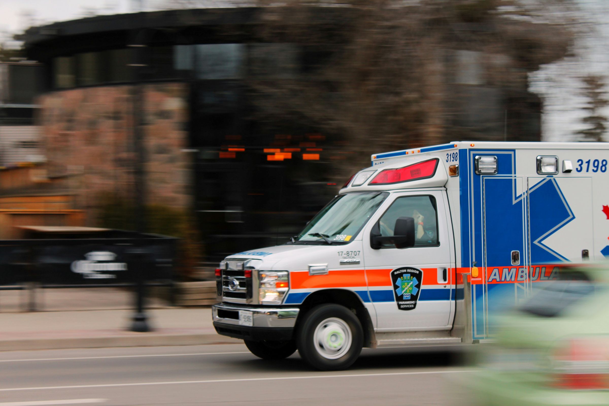 A white and blue ambulance drives quickly down a city street, conveying urgency. Motion blur accentuates the vehicle's rapid speed.